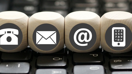 Holzwürfel mit Symbolen zu Telefon, Mail, Internet und Smartphone stehen auf einer Tastatur
