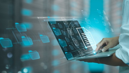 Seitliche Aufnahme einer Person, die einen Laptop hält. Auf dem Bildschirm sind mehrere Icons von Ordnern. Über der Tastatur ist das Icon eines Dokuments