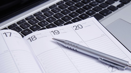 Detailansicht Terminkalender mit Stift, im Hintergrund Computertastatur