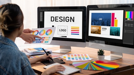 Designteam sitzt vor zwei Bildschirmen und bespricht Farben für ein Firmenlogo