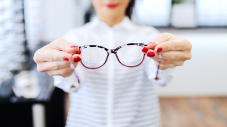 Person in Optikfachhandel bietet Brille zur Anprobe an