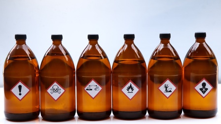 Braune Glasflaschen mit schwarzen Plastikverschlüssen nebeneinander auf weißem Hintergrund mit weißen quadratischen Etiketten mit roter Umrandung und verschiedenen schwarzen Warnsymbolen: Rufzeichen, Totenkopf, Flammen und dergleichen