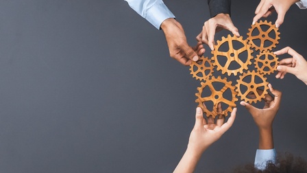 Sechs Hände von sechs Personen halten sechs unterschiedlich große Zahnräder nebeneinander