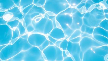 Nahaufnahme von Wasser. Der Untergrund ist blau mit gebrochenen Lichtreflexionen.