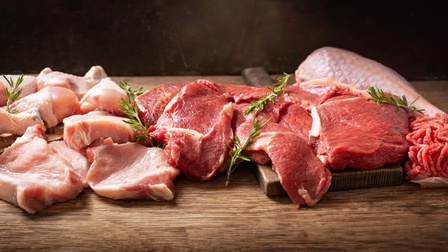 Auf einem Holztisch liegen verschiedene Fleischteile, wie Keule oder Brust sowie ein Stück faschiertes Fleisch. Auf dem Fleisch liegen teilweise Rosmarinzweige