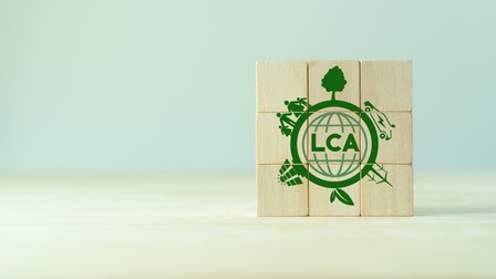 Neun Holzwürfel in Dreierreihen übereinander positioniert mit grünem Schriftzug LCA umrandet von Symbolen zur Nachhaltigkeit wie Windräder, Solaranlagen und Pflanzen.