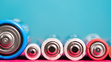 Detailansicht nebeneinander liegender Batterien in unterschiedlichen Größen vor türkisblauem Hintergrund