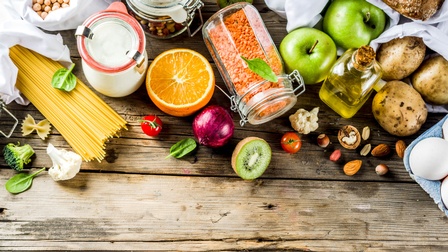 Gemüse, Obst und Nudeln liegen drapiert in Gläsern oder weißen Vorratssäckchen auf einem Holzuntergrund, Konzept Zero Waste
