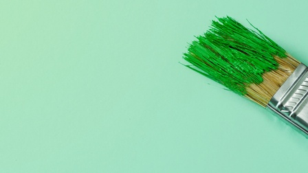 Nahaufnahme eines Pinsels auf einem grünen Hintergrund, die Pinselspitzen sind mit grüner Farbe bedeckt.