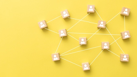 Netzwerk aus Holzwürfel mit Personenicon und verbindenden Linien vor einem gelben Hintergrund