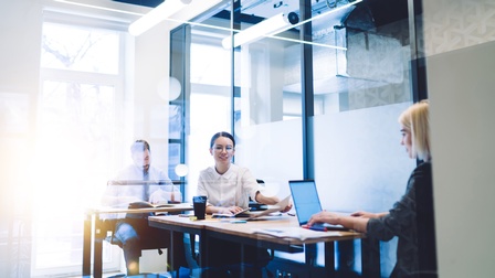 Mehrere Personen sitzen in Arbeitszimmer und verrichten Computerarbeit