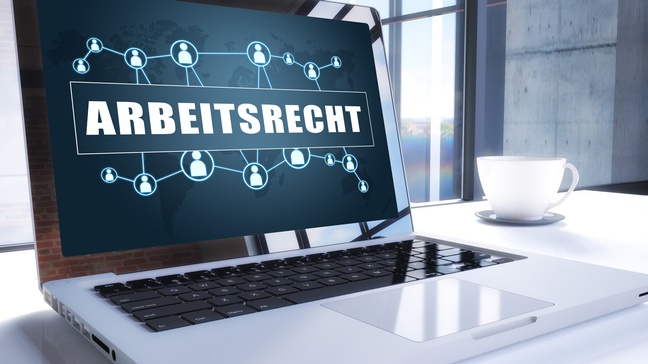 Aufgeklappter Laptop mit Schriftzug Arbeitsrecht und Personenicons am Bildschirm, daneben weiße Tasse stehend 