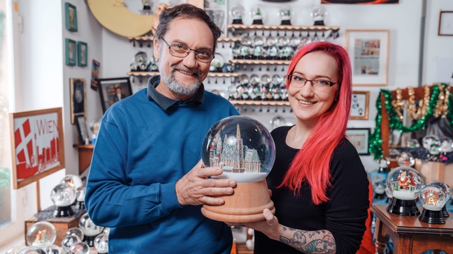 Zwei lächelnde Personen mit Brillen halten große Schneekugel in Händen