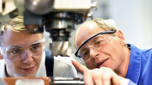 Zwei Personen mit Schutzbrillen inspizieren CNC-Maschine