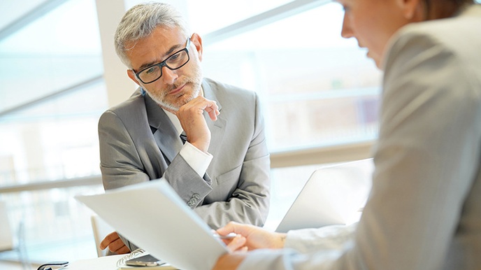 Zwei Personen sitzen an Tisch und blicken auf Dokument