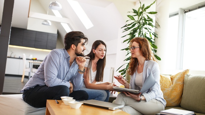 Drei Personen sitzen an Couchtisch in Wohnung und unterhalten sich