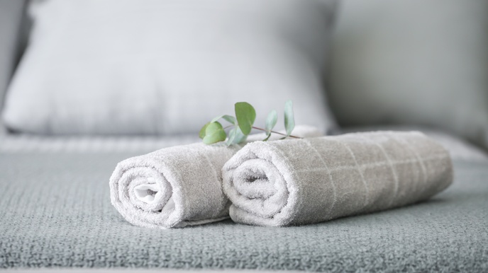 Zwei eingerollte, hellgraue Handtücher auf einem Bett
