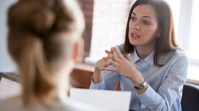 Person mit langen dunklen Haaren, hellblauer Bluse und silberner Uhr spricht mit anderen Personen in der Unschärfe