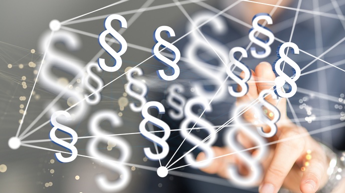 Nahaufnahme einer Person, die mit dem linken Zeigefinger auf eine Scheibe tippt. Auf der Scheibe sind weiße Symbole von Paragraphen, sowie Linien, die von weißen Punkten ausgehen. Im Hintergrund sind gelbe Punkte