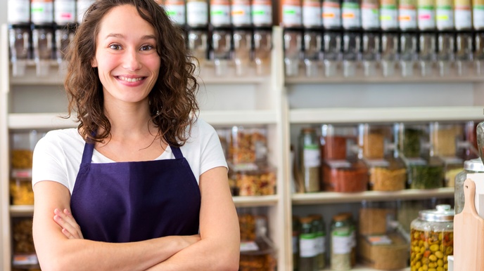 Sympathische Unternehmerin in Schürze lächelt in ihrer Greißlerei