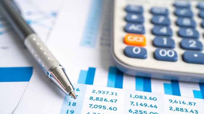 Detailansicht eines Blattes mit eines Zahlen und statistischem Diagramm, darauf deutend Spitze eines Kugelschreibers und Taschenrechner darauf liegend im Ausschnitt