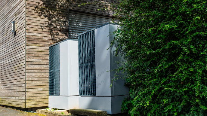 Zwei graue Schränke mit Gittern zwischen hölzerner Hausfassade und grün belaubter Hecke