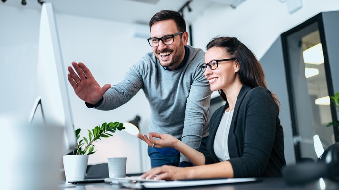 Personen mit Brillen blicken freudig auf einen Bildschirmmonitor in einem hellen, modernen Büro 