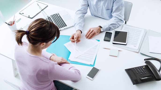 Besprechungssituation mit zwei Personen im Fokus, die Unterlagen an einem Schreibtisch betrachten