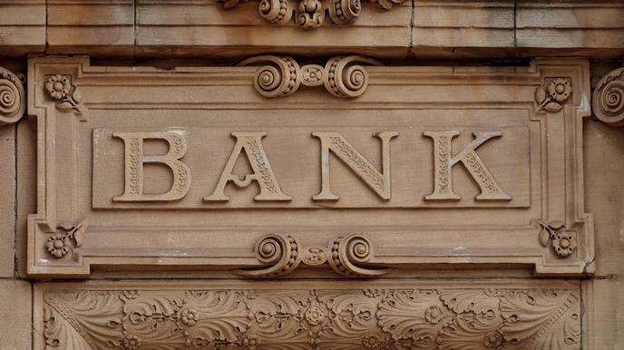 Detailansicht eines historischen braungrauen Türgiebels mit Stuckaturelementen, mittig im Fokus Schriftzug Bank