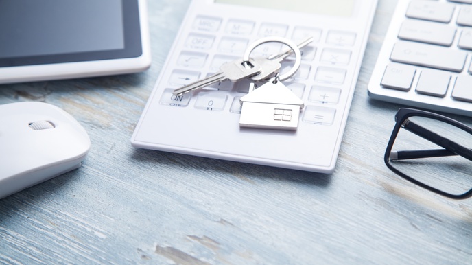 Schlüsselbund liegt auf einem Taschenrechner, während ein Tablet, eine Maus, eine Tastatur sowie eine Brille ebenso am Tisch liegen