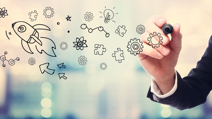 Hand in Businesskleidung zeichnet ein Ideenkonzept auf eine Glasscheibe, im Hintergrund zeigt sich ein Bokeh