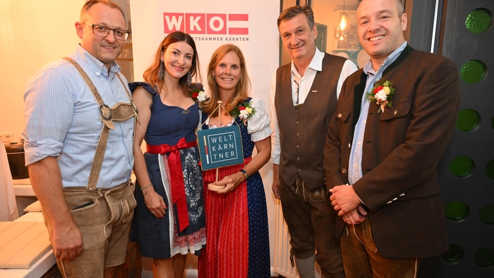 WKO Kärnten: Vier Personen in Tracht halten ein Schild mit "Weltpartner"