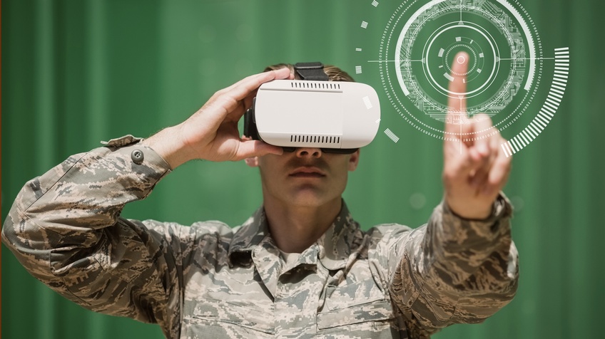 Eine Person in einer Militäruniform trägt eine VR-Brille auf dem Kopf und berührt mit dem linken Zeigefinger eine virtuelle Zielscheibe