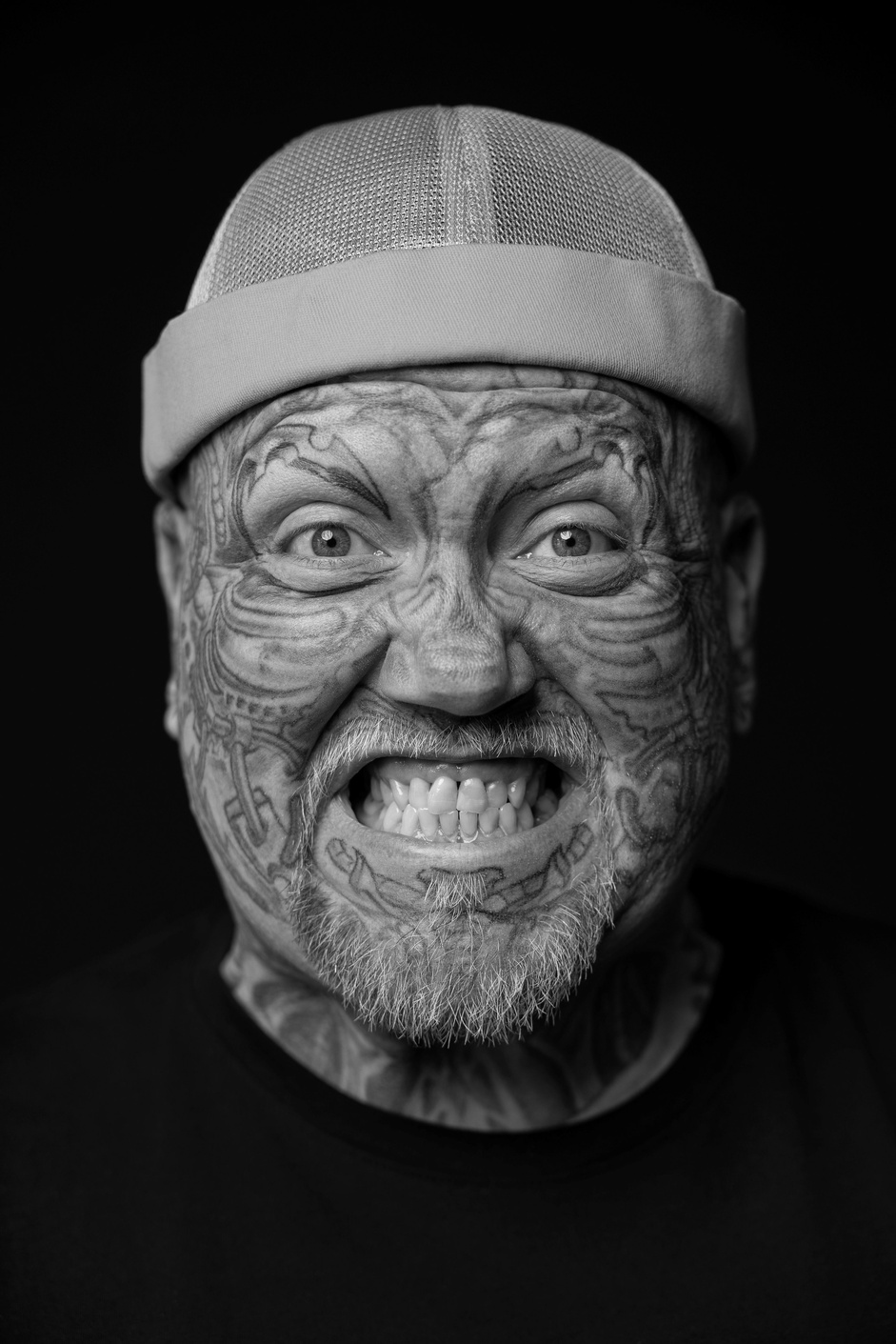 Porträt einer Person mit Gesichtstätowierungen und heller Mütze.