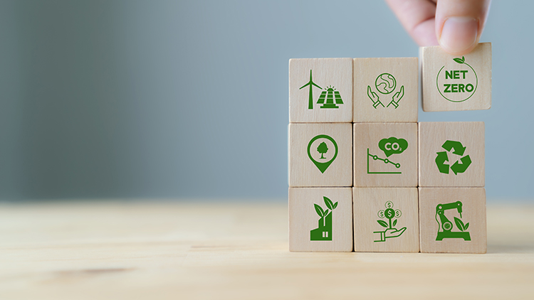 Hand platziert Holzwürfel aufeinander, auf den Würfeln Symbole zu Nachhaltigkeit