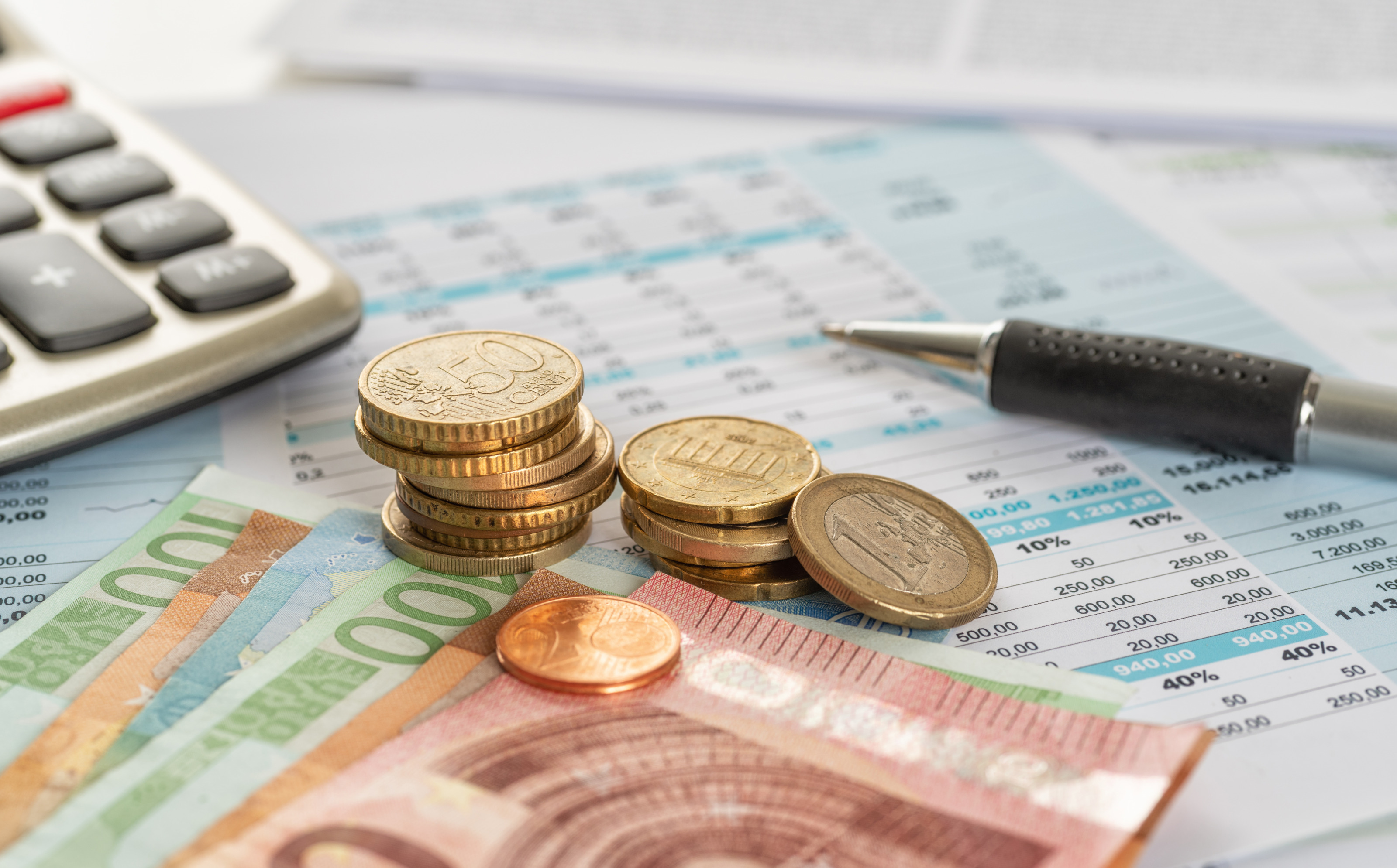 Detailansicht Euroscheine und -m&uuml;nzen auf Dokumenten liegend, daneben Taschenrechner und Kugelschreiber