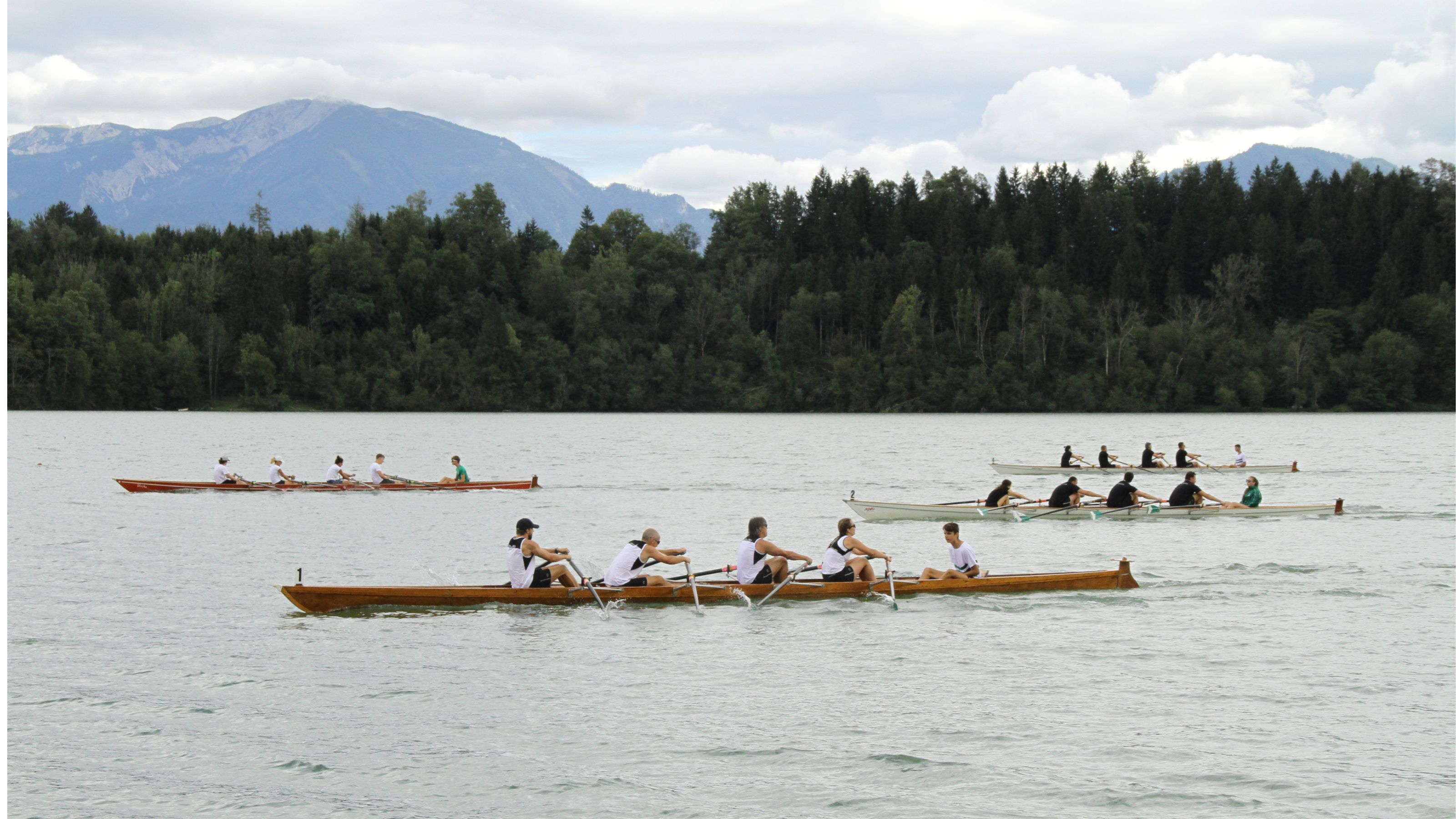 Stausee mit Ruderbooten sowie Wald und Berg im Hintergrund