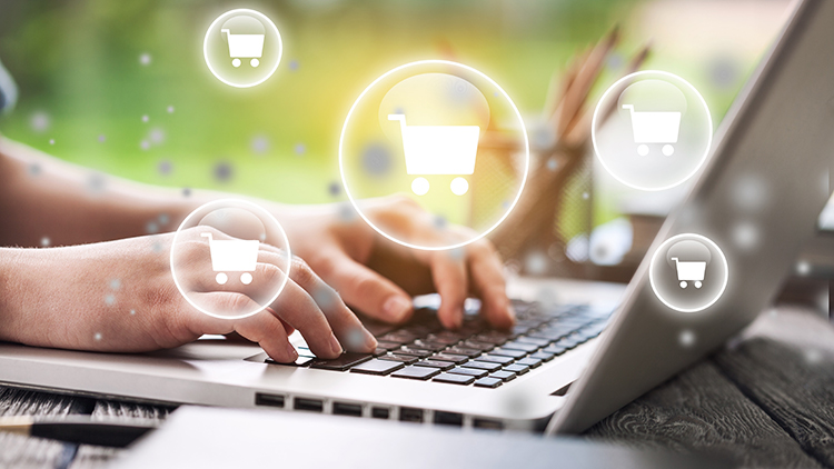 Hände tippend auf Notebook-Tastatur, darüber leuchtende Einkaufswägen