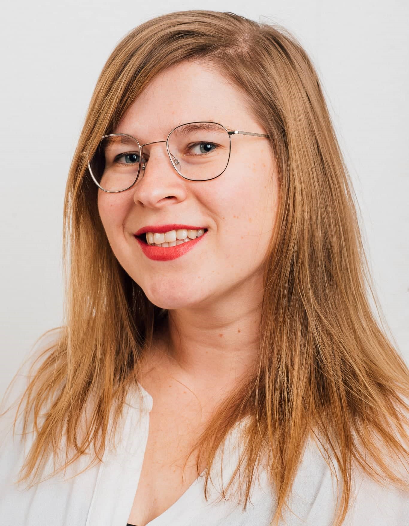 Portr&auml;tfoto: Person mit langen Haaren, Brille und rotem Lippenstift vor hellem Hintergrund