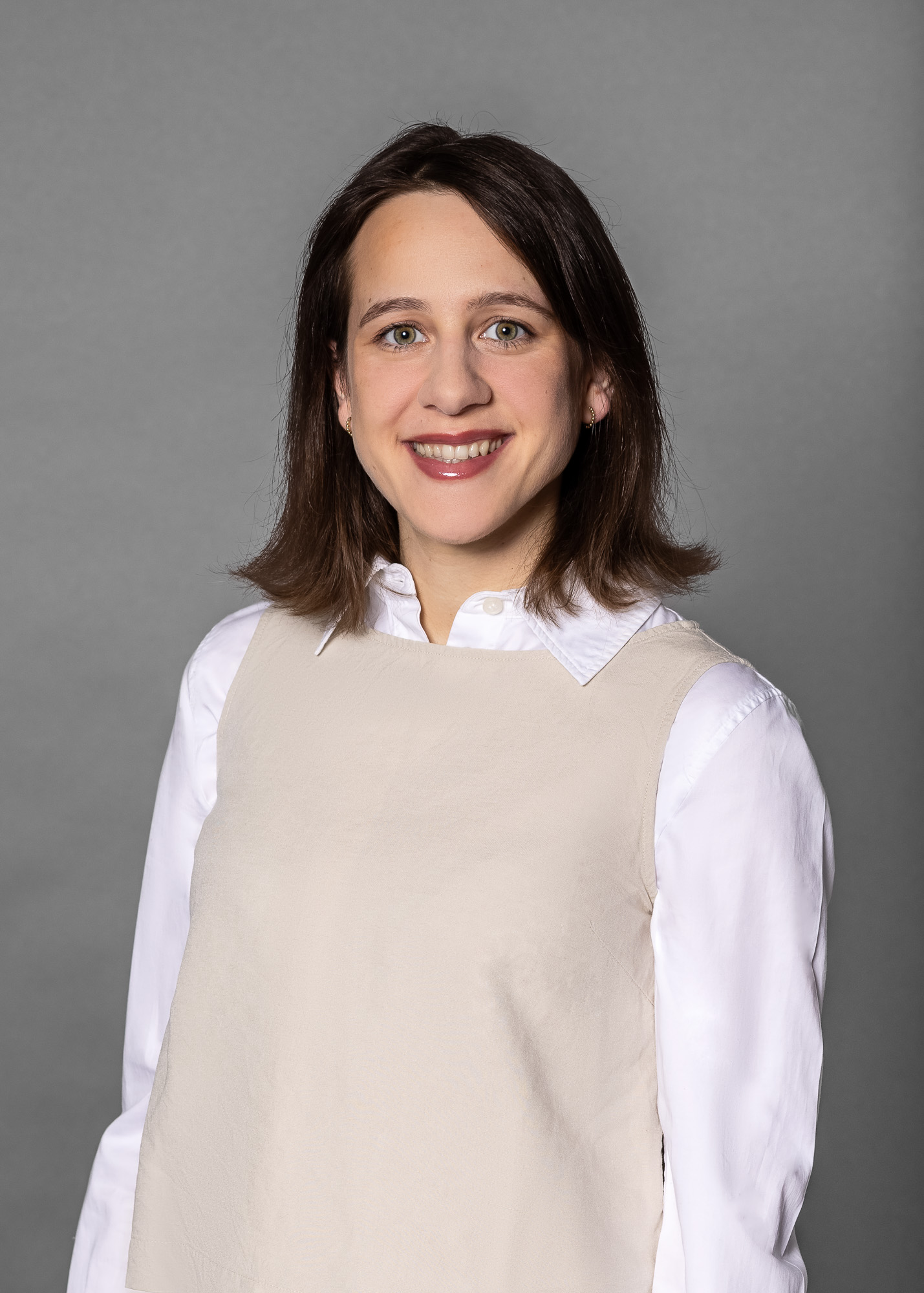Portrait einer Person mit wei&szlig;er Bluse und hellem Oberteil vor grauem Hintergrund