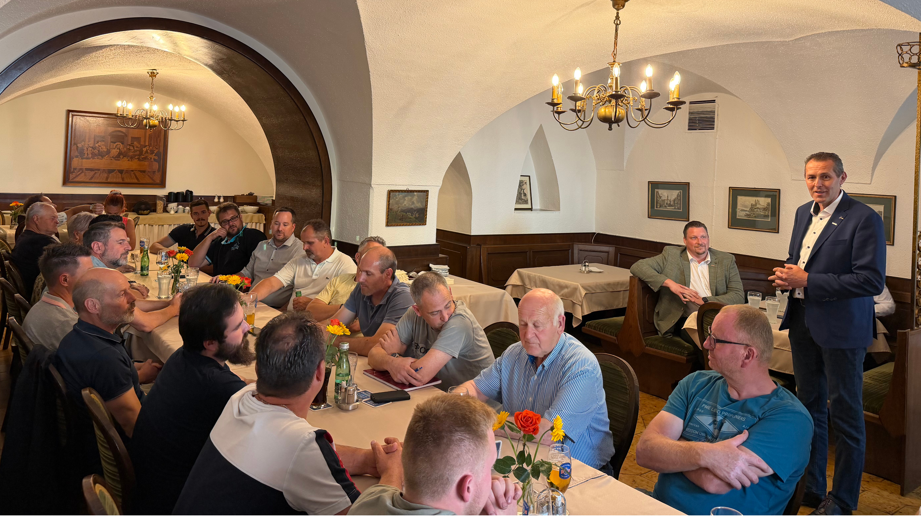Personen an einem langen Tisch in einem gew&ouml;lbeartigen Kellerraum