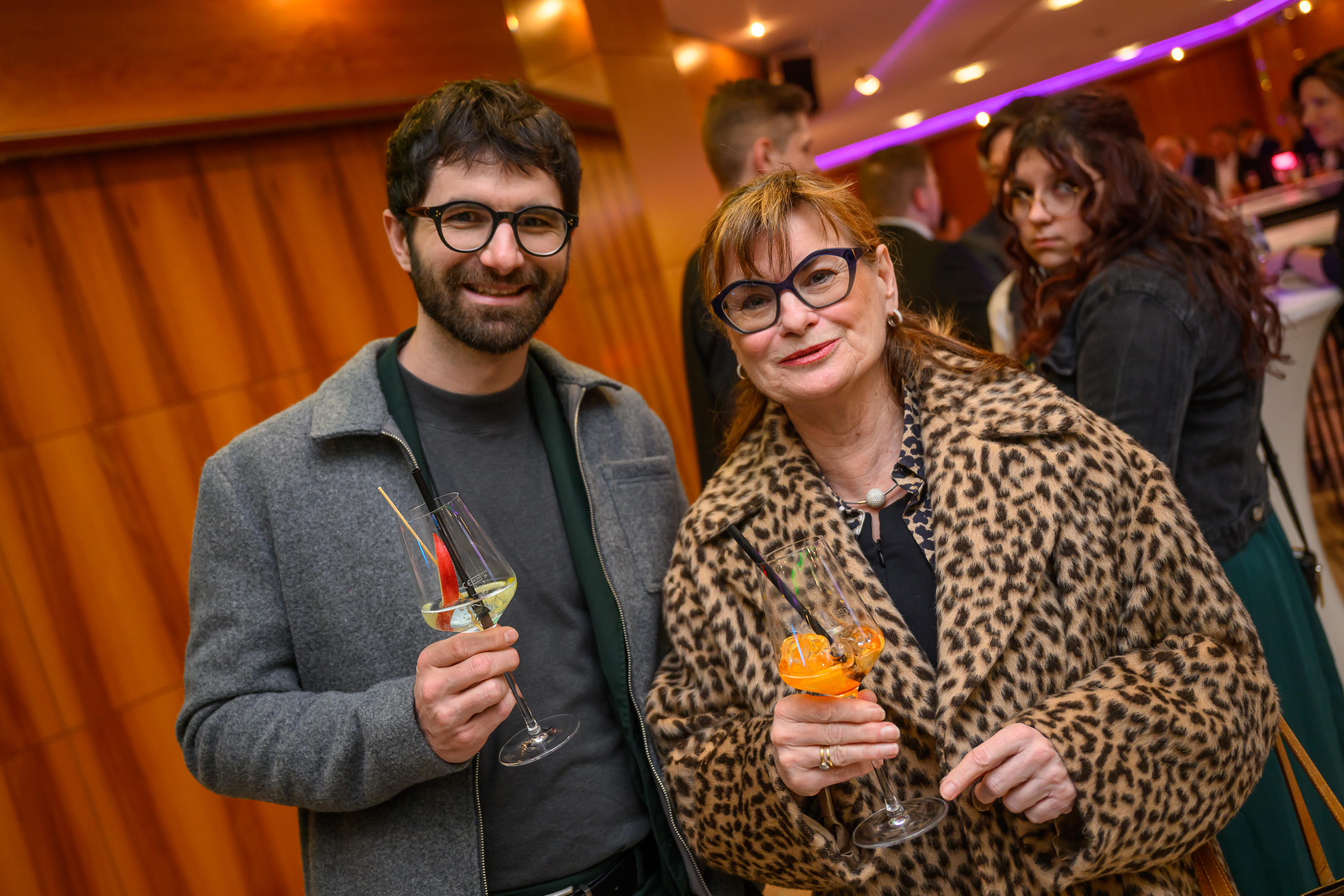 ein Mann in grauer Kleidung und eine Frau in Leopardenjacke, beide mit Brille