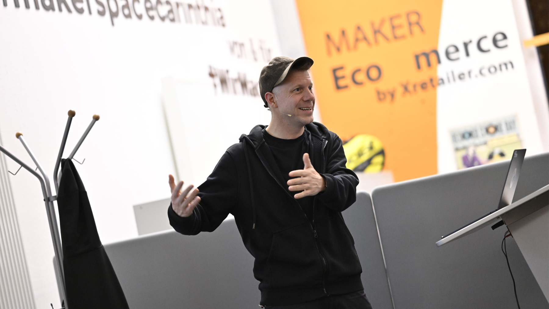 Mann mit Schirmkappe auf einer Bühne gestikuliert mit seinen Händen