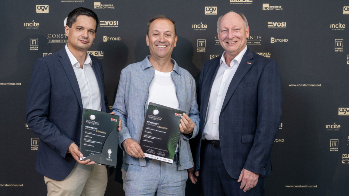 Drei M&auml;nner stehen vor einer Constantinus-Award-Fotowand. Zwei von ihnen halten Nominierungsurkunden f&uuml;r K&auml;rnten in die Kamera.