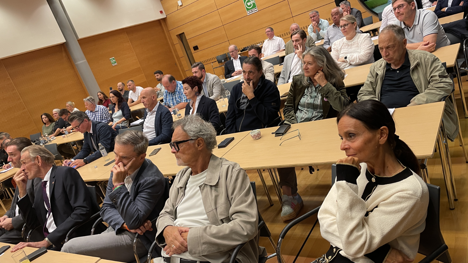 Zuschauer sitzen in einem Saal vor Tischen