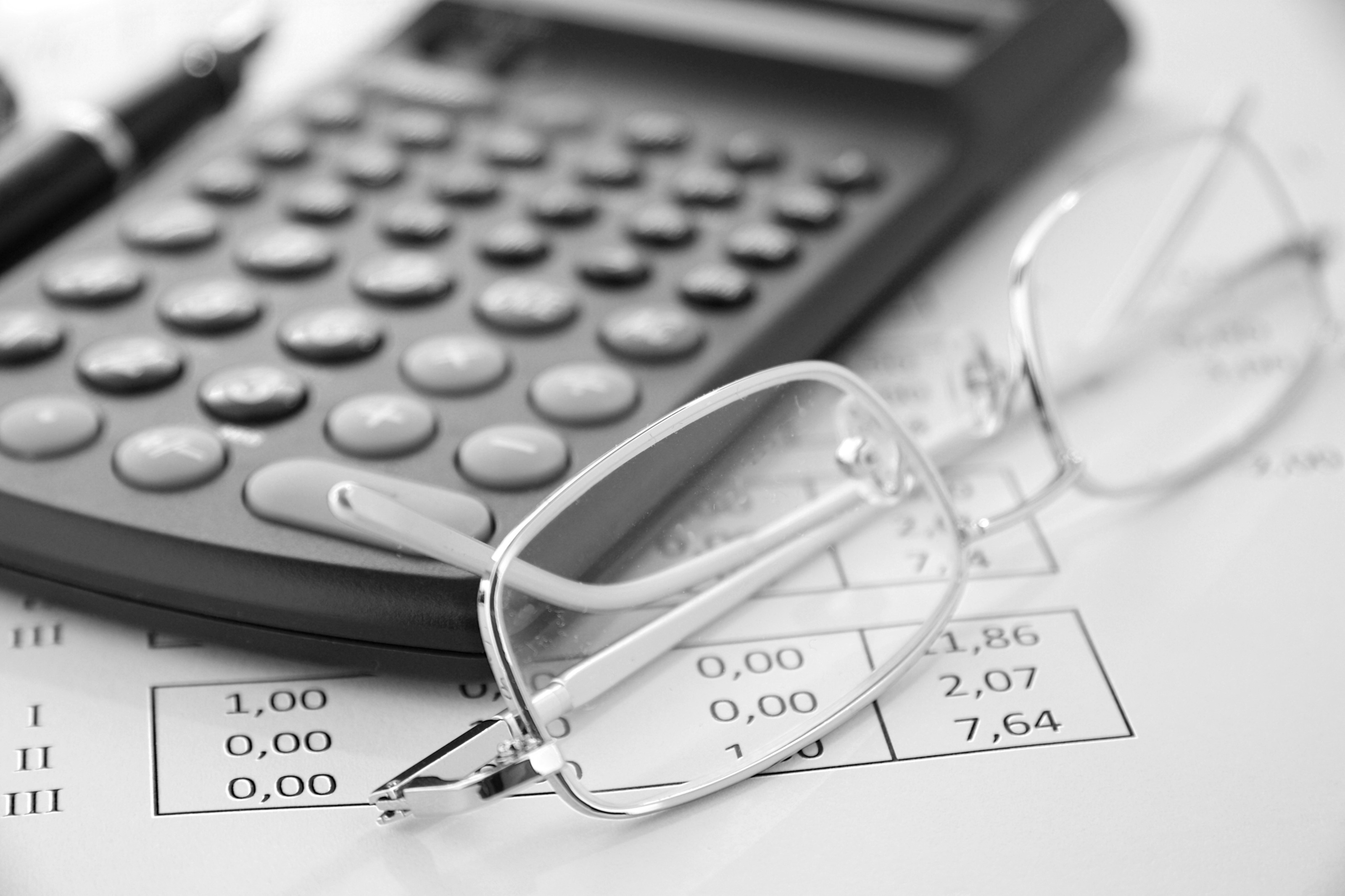 Detailansicht Brille neben Taschenrechner auf Papier mit Zahlen liegend