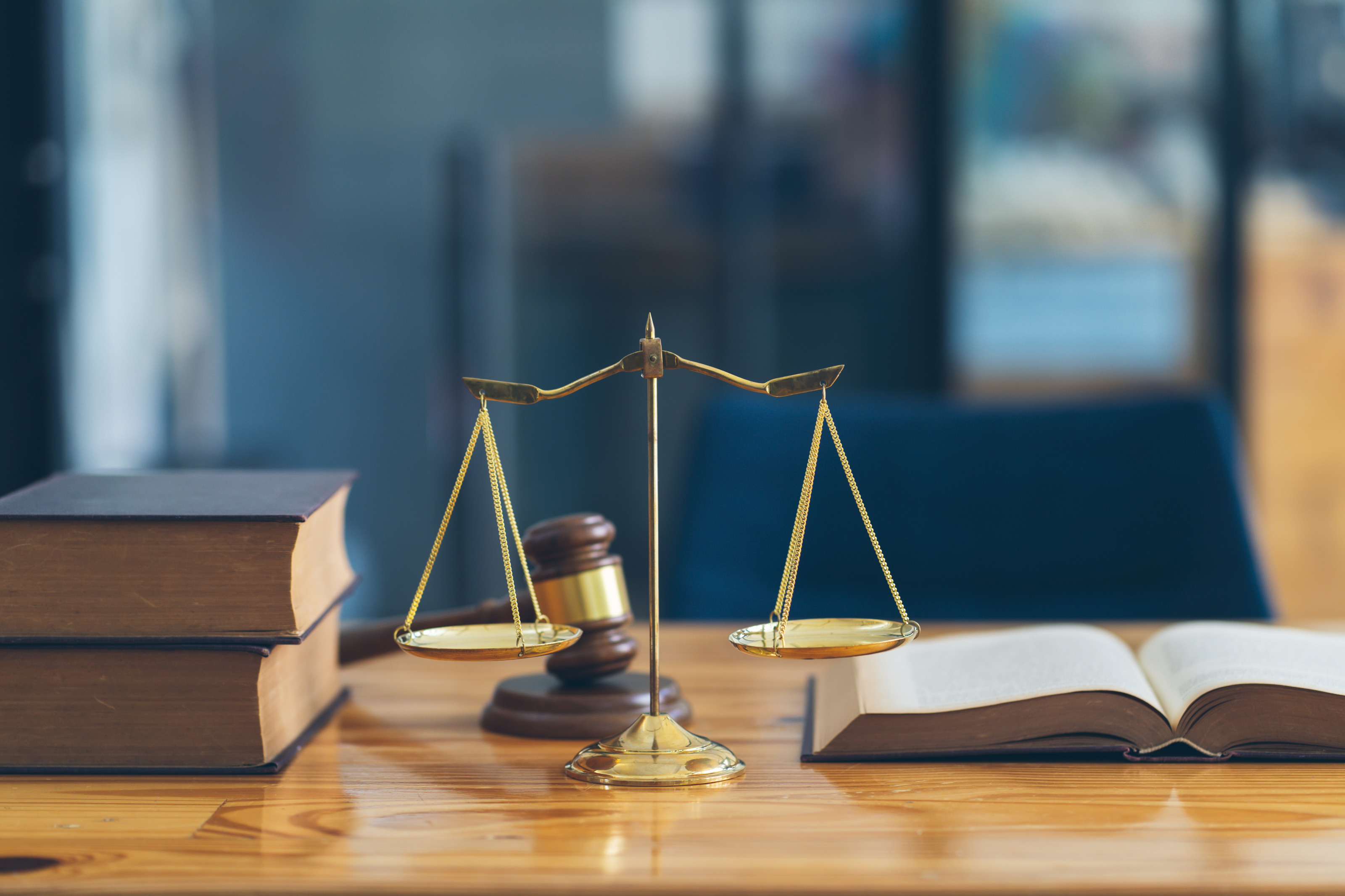 B&uuml;cher sowie ein Richterhammer, eine goldene Waage und ein aufgeschlagenes Buch auf einem Holztisch