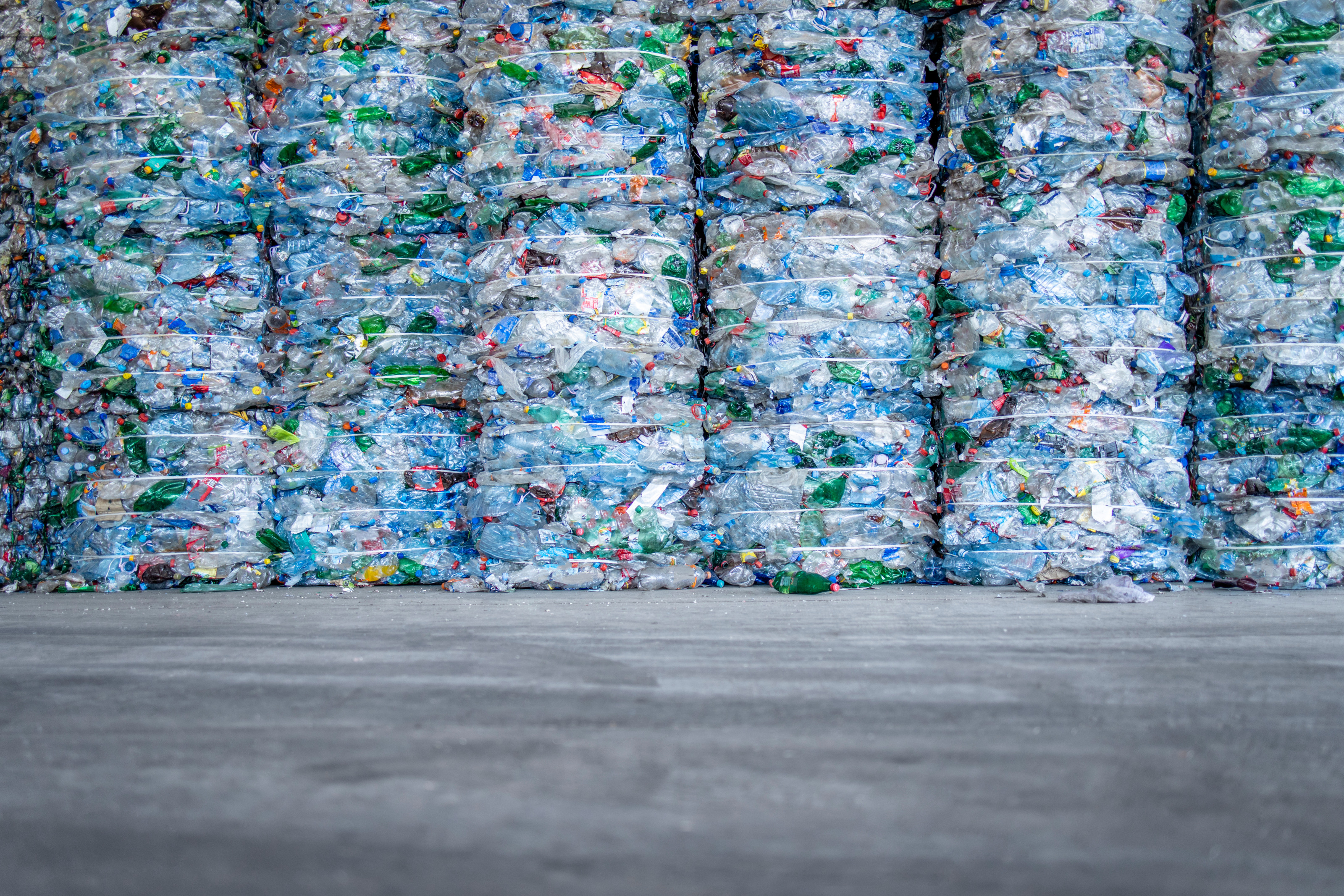 Mehrere Stapel gepresster Plastikflaschen nebeneinander stehend auf Betonboden