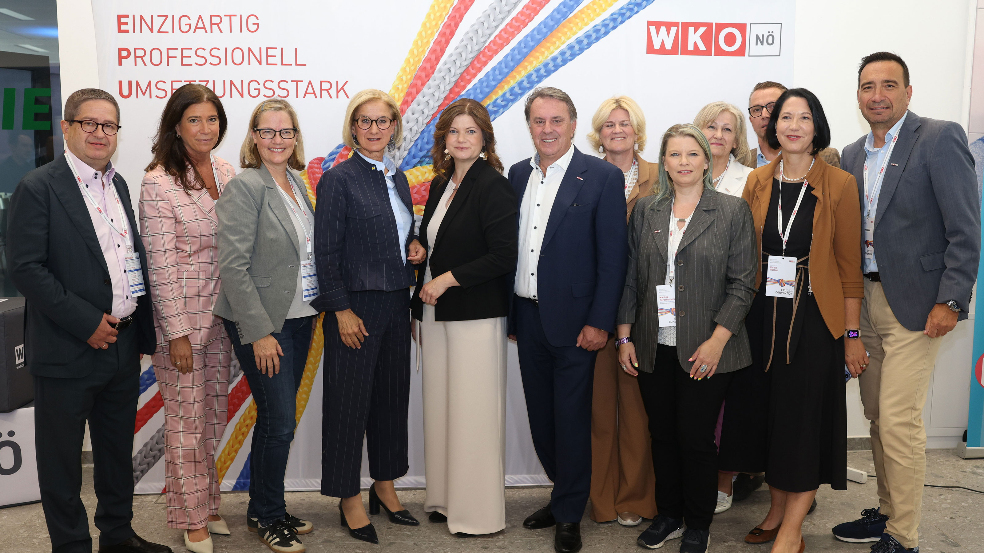 Mehrere Personen posieren gemeinsam vor einer WKO-N&Ouml; Fotowand mit buntem Seilmotiv und Veranstaltungshinweis zur EPU Convention 2026.