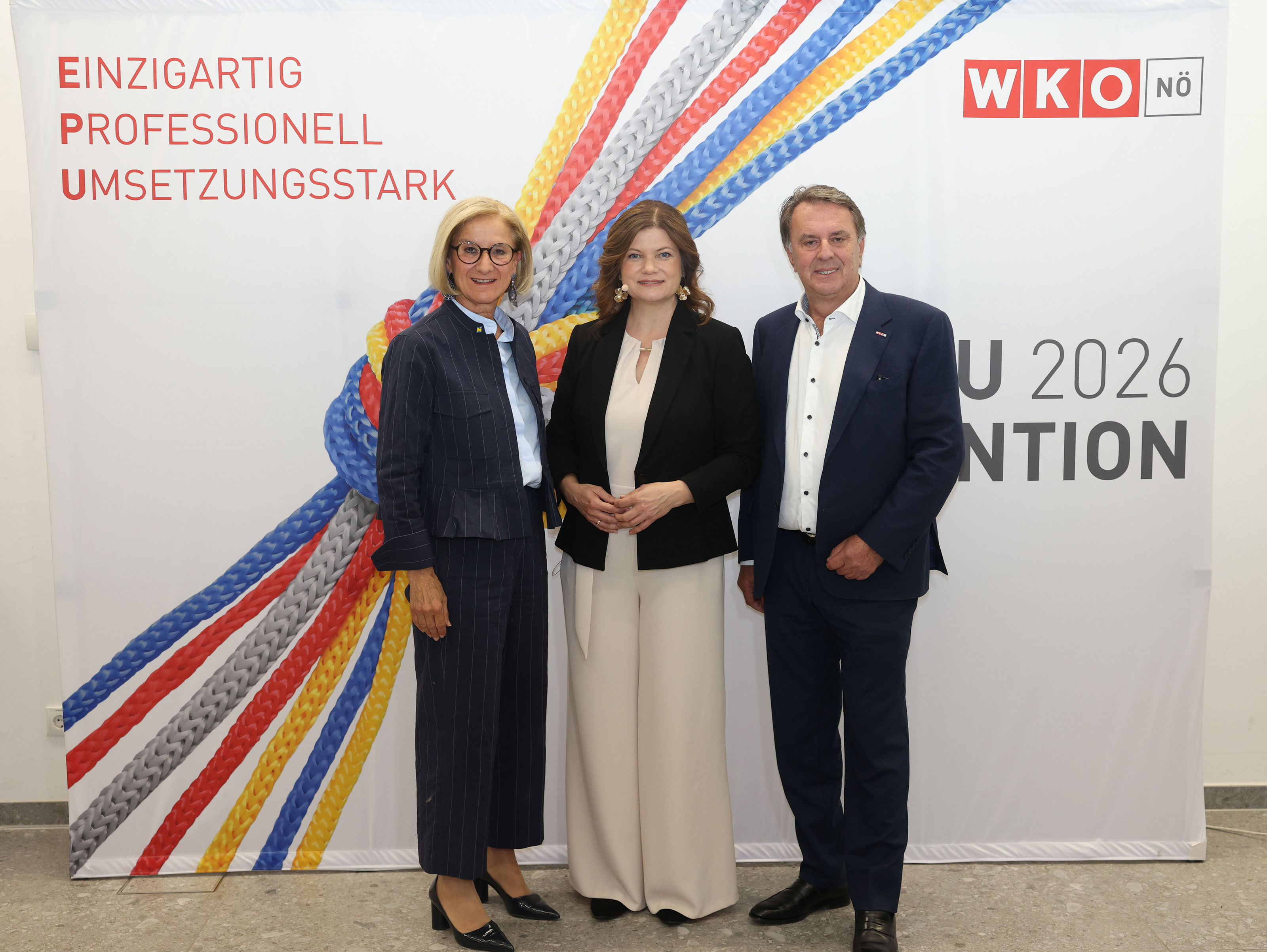 Drei Personen stehen vor einer WKO-N&Ouml; Fotowand mit buntem Seilmotiv und dem Text &bdquo;Einzigartig, professionell, umsetzungsstark&ldquo; bei der EPU Convention 2026.